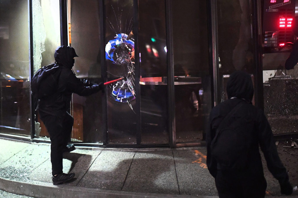 A rioter smashes a window at a Mechanics Bank branch in Berkeley, California. (Photo: Noah Berger/EPA/Newscom) 