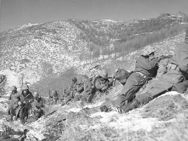 Marines under the cover of a large boulder engaging the Chinese. (Photo: Wikimedia)