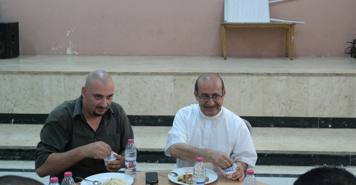 Father Khalil Jaar (right) shares a meal with refugees and neighbors in the parish hall at St. Mary's in Marka, Jordan. (Photo: Charlotte Florance/The Daily Signal)