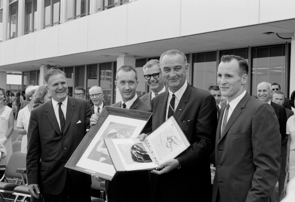 President Johnson holds a Gemini-4 souvenir photo album which he was presented by Gemini-4 astronauts James A. McDivitt and Edward H. White II. McDivitt holds a framed picture of White's "spacewalk" which was also given the President. (Photo: NASA)