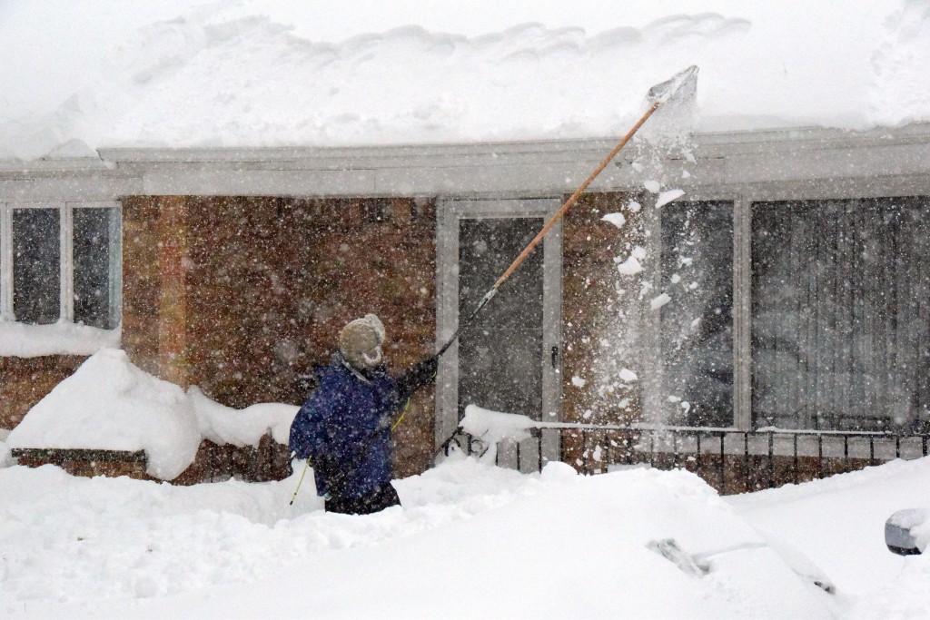 A man uses a long fishing net to scrape snow off his roof as snow continues to fall. (Photo: Newscom)