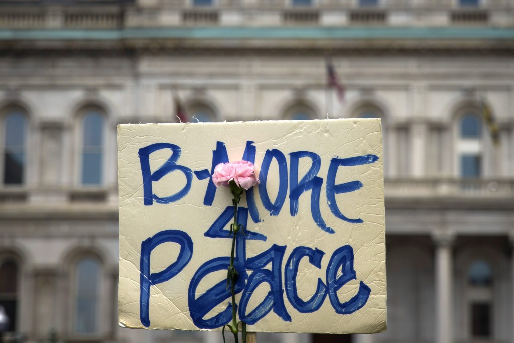 A flower is taped on a protest sign during a rally at City Hall in Baltimore (Photo: Newscom)