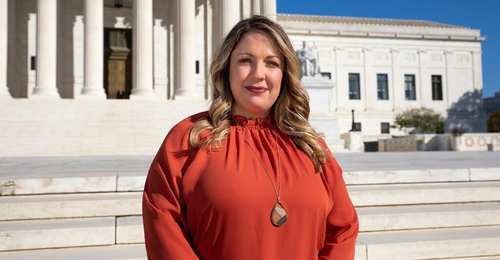 Lorie Smith in red stands before the Supreme Court