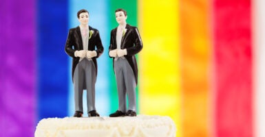 Two men in suits on a cake-topper with a rainbow flag in the background.