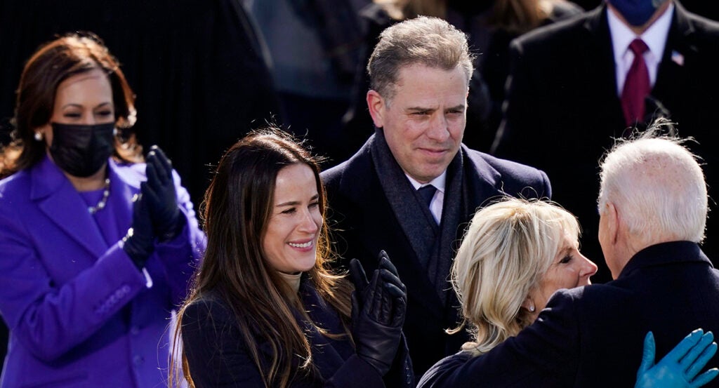 Hunter Biden in a suit looks on as Jill Biden embraces Joe Biden and Kamala Harris in a blue pantsuit claps enthusiastically