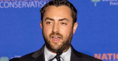 Josh Hammer in a suit in front of a blue background.