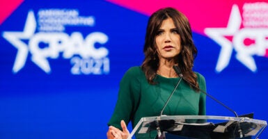 South Dakota Gov. Kristi Noem in a blue suit in front of an American flag.