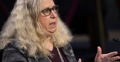 Man with long blond hair and glasses speaks in front of a microphone