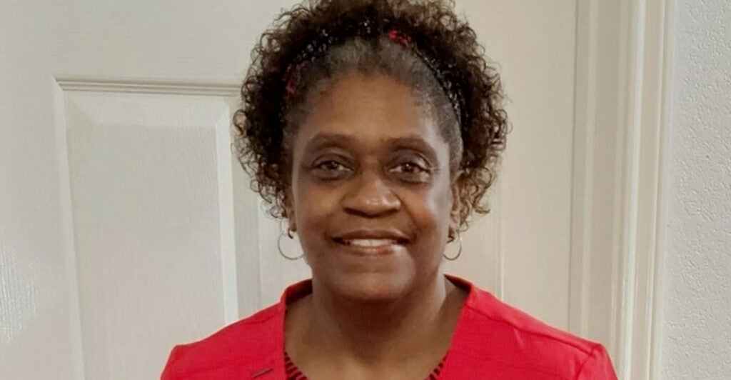 Black woman in a red outfit smiles in front of a white door