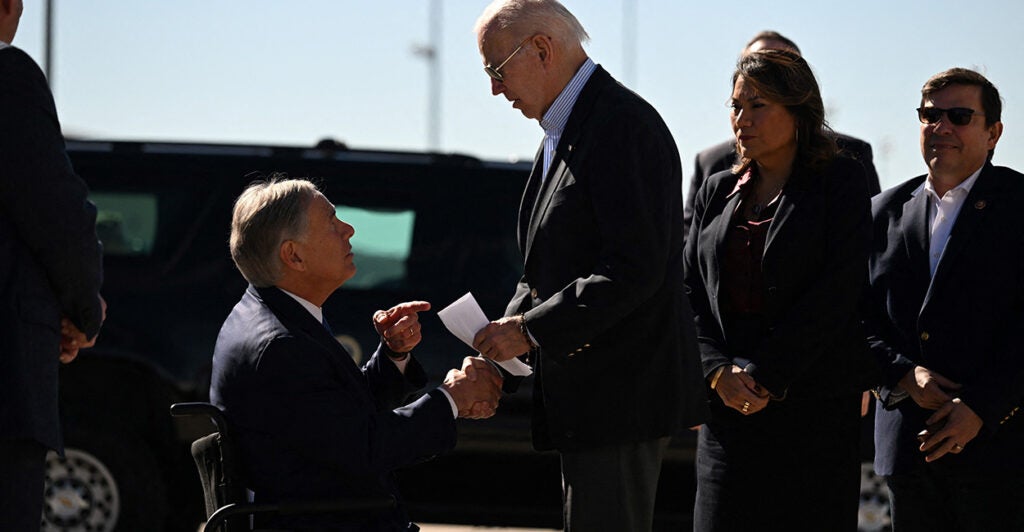 Greg Abbott hands Joe Biden a letter as both men stand in suits