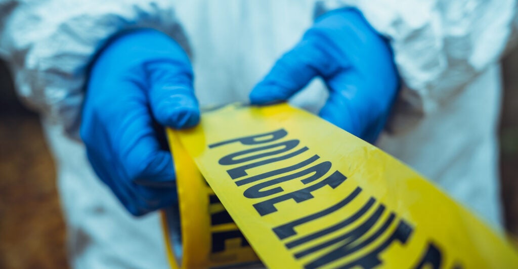 person in protective blue and white suit unfurls police tape