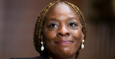 Black lady smiles with white earrings and braided blonde hair