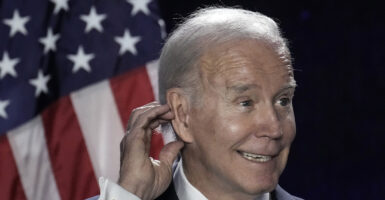 Joe Biden scratching ear in front of an American flag