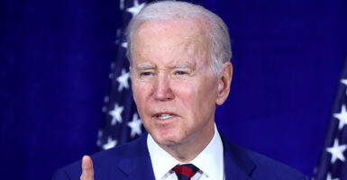 President Joe Biden in a blue suit with a blue background and American flags