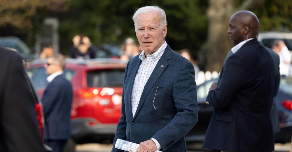 President Joe Biden wearing a suit coat and button down shirt looks strait ahead while standing outside.