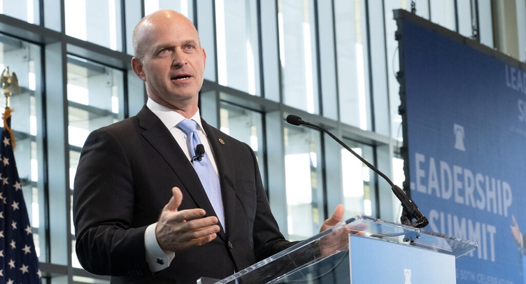 Heritage Foundation President Kevin Roberts, in a black suit with a blue tie, speaks in front of a backdrop reading "Leadership Summit"