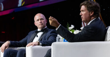 Kevin Roberts in black tie listens as Fox News host Tucker Carlson gestures.