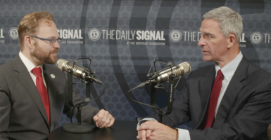 The Daily Signal's Tyler O'Neil in a grey suit and red tie listens as former Virginia Attorney General Ken Cuccinelli speaks in a pin-stripe suit and red tie