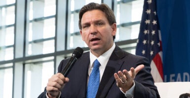 Florida Gov. Ron DeSantis in a black suit with a blue tie in front of an American flag