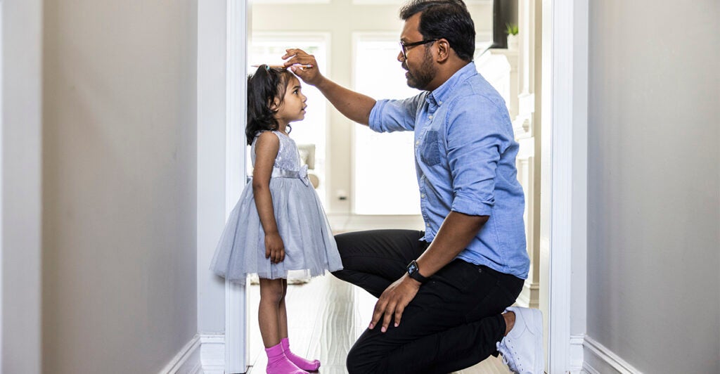 Father measuring height of 5-year-old daughter