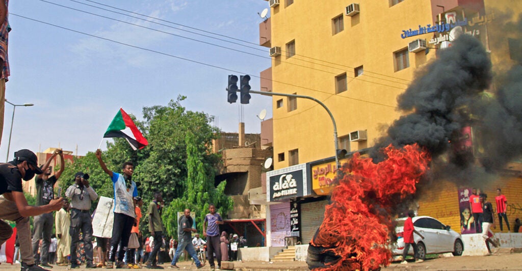 Sudanese demonstrators lift flags and burn tires during a rally to demand the return to civilian rule