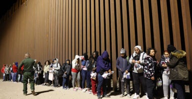 Illegal aliens line up along a section of border wall.