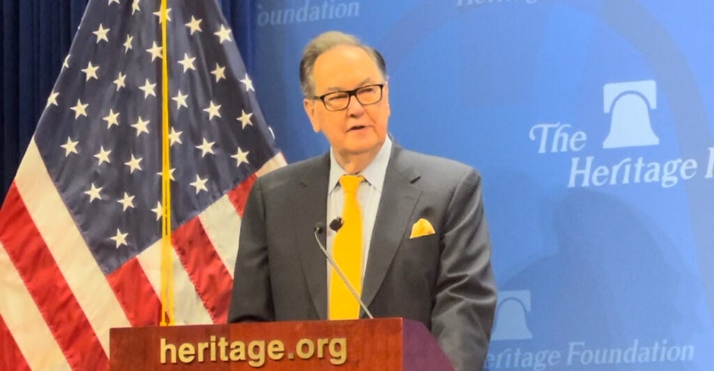 Cal Thomas speaks from a podium in a dark suit and yellow tie.