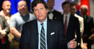 Tucker Carlson speaks to a crowd wearing a dark suit.