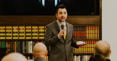 Lucas Miles in a grey suit speaks while holding a microphone