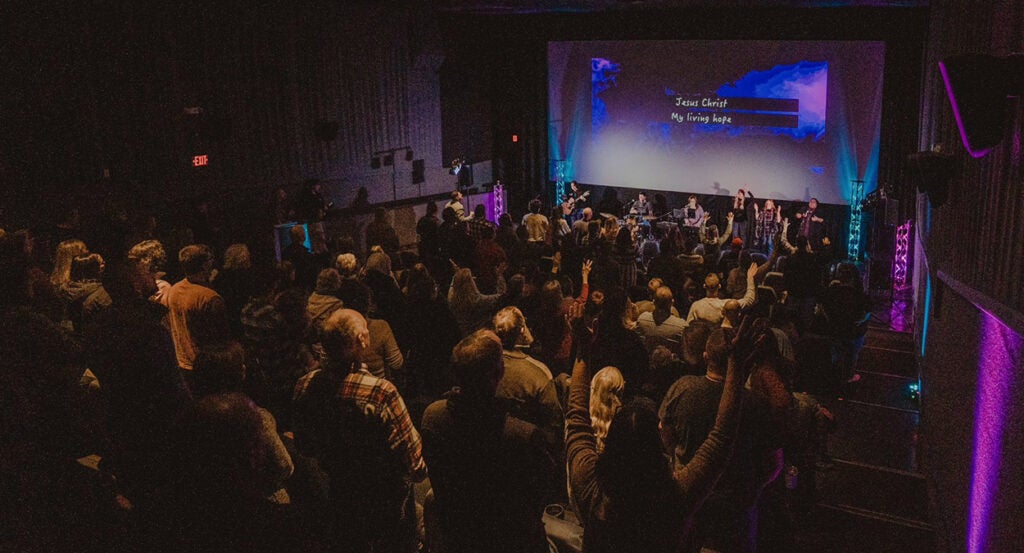 Christians gather for worship in a movie theater at The Pines Church