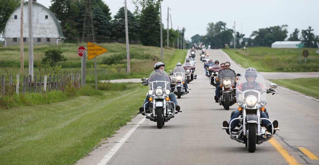 A large group of motorcyclists ride down the street.