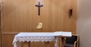 Glass-covered candle burns to the right of a crucifix in a chapel.