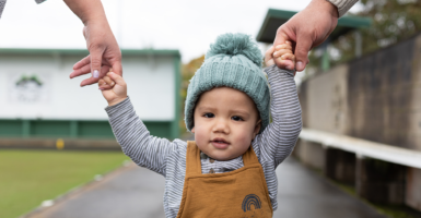 Walking Toddler holds parents' hands.