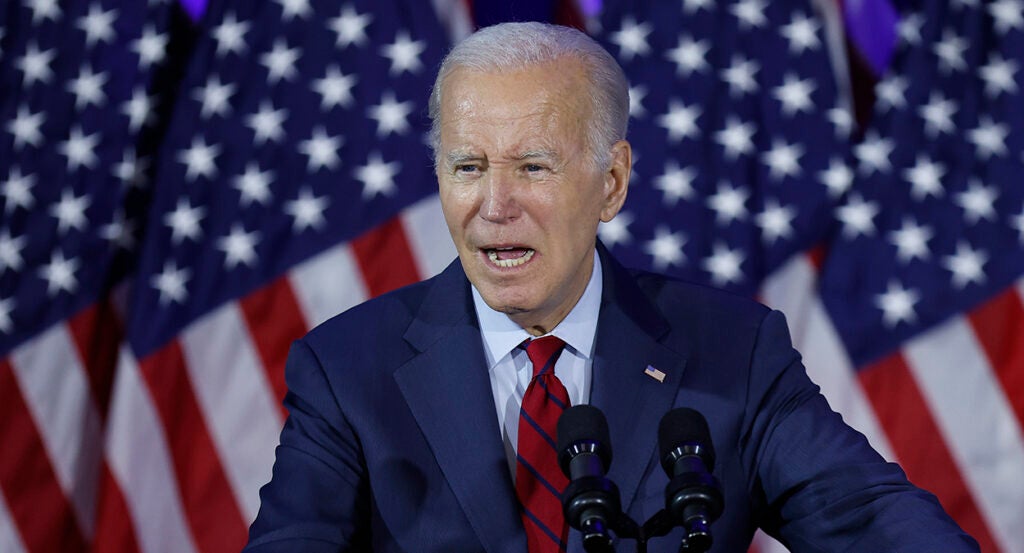 Joe Biden speaks in a blue suit in front of American flags