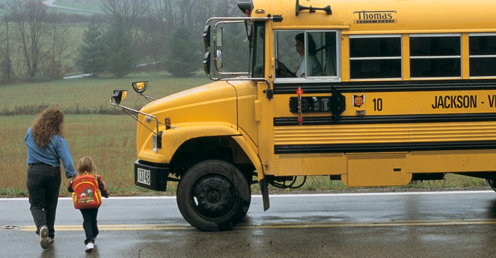 Mom walks her child to a yellow school bus.