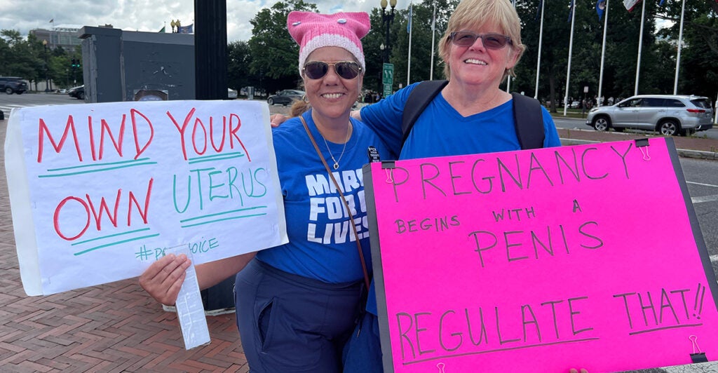 Two women, one in a pink hat, hold signs in support of abortion.