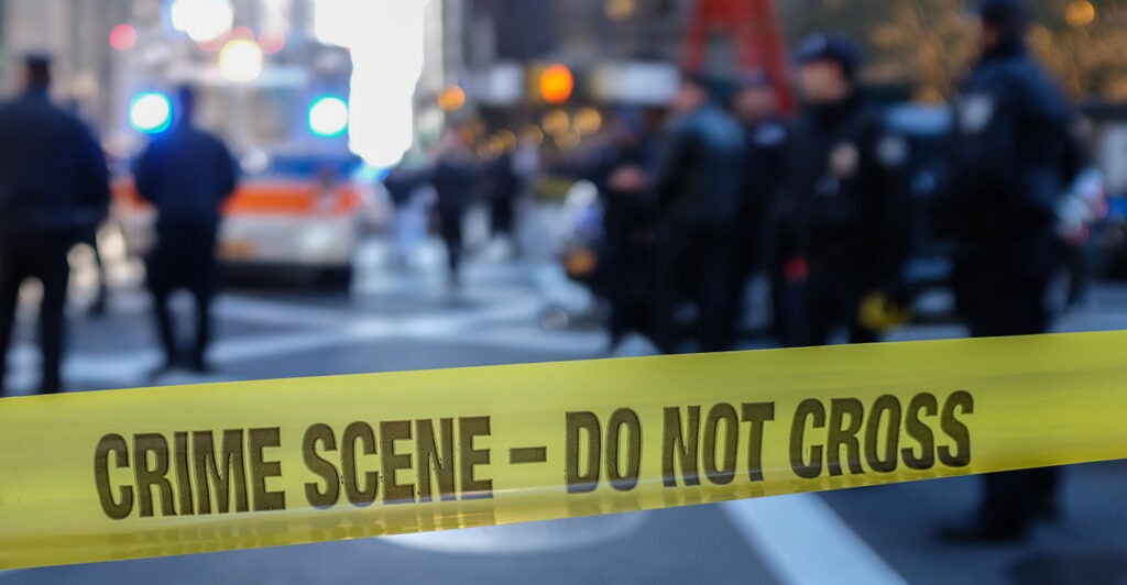 Yellow crime scene take blacks a road. Police officers and lights are seen is the background.