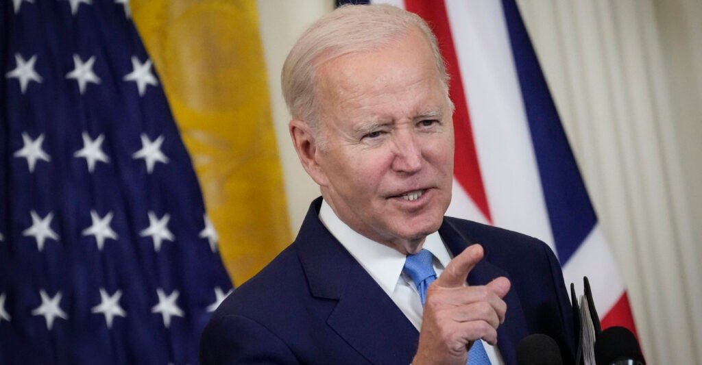 Joe Biden gestures in a suit in front of an American flag