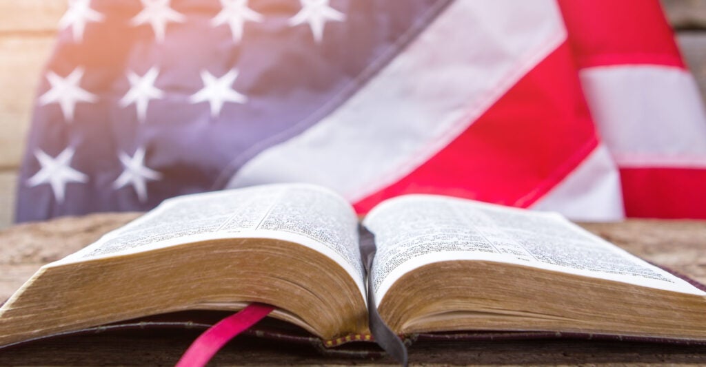 An open book sits on a table with an American flag behind it.