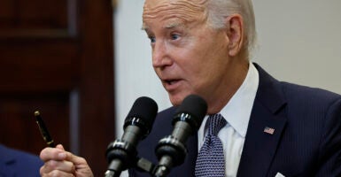 Joe Biden in a suit with a blue tie holds a pen