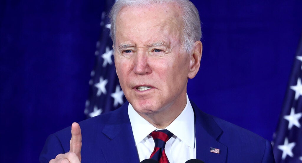 Joe Biden in a blue suit with an American flag pin raises a finger