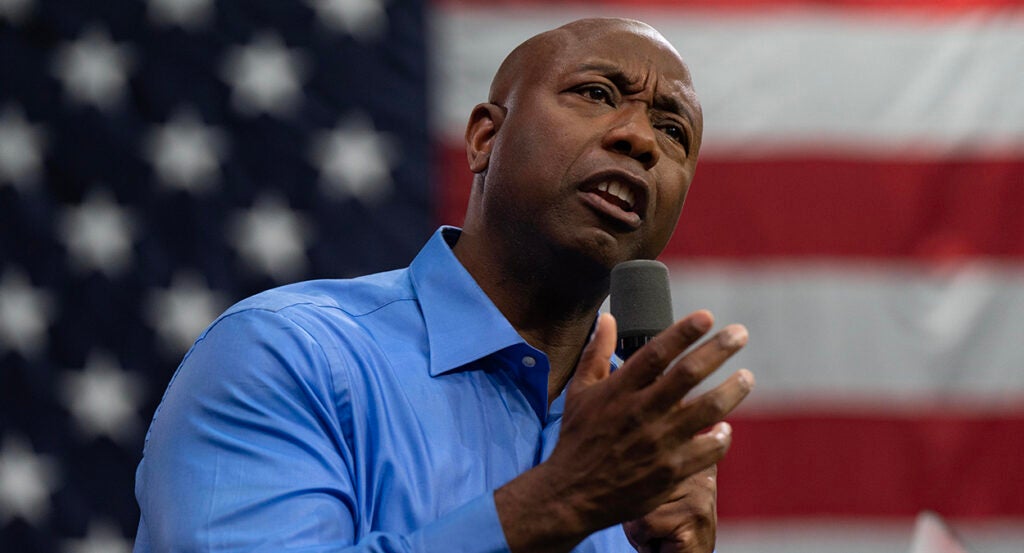 Tim Scott in a blue shirt gestures before an American flag