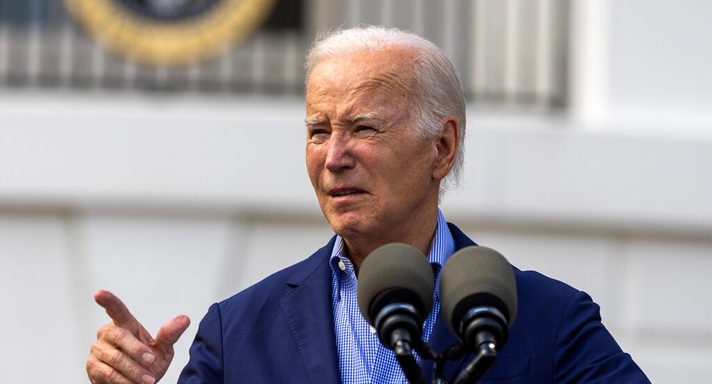 Joe Biden in a blue shirt and a blue suit jacket points to the right, looking bewildered