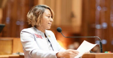 Mesha Mainor speaks into a microphone holding a paper and wearing a light suit jacket.