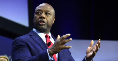 Sen. Tim Scott speaks from stage in a dark blue suit and red tie.