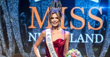 Trans model poses in a red dress, a sash that says 