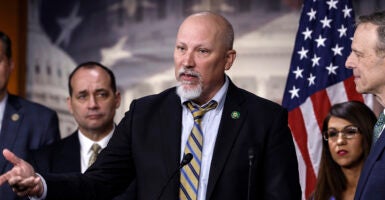 Chip Roy, bald and with a goatee, gestures in a black suit with a multi-colored striped tie