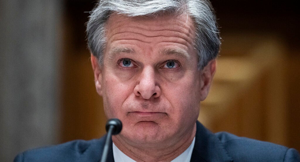 FBI Director Chris Wray looks forward in a suit