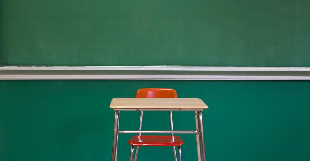 A single desk sits in front of a chalkboard.