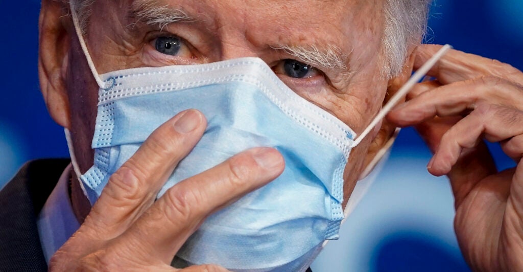 Joe Biden holds a blue mask over his face